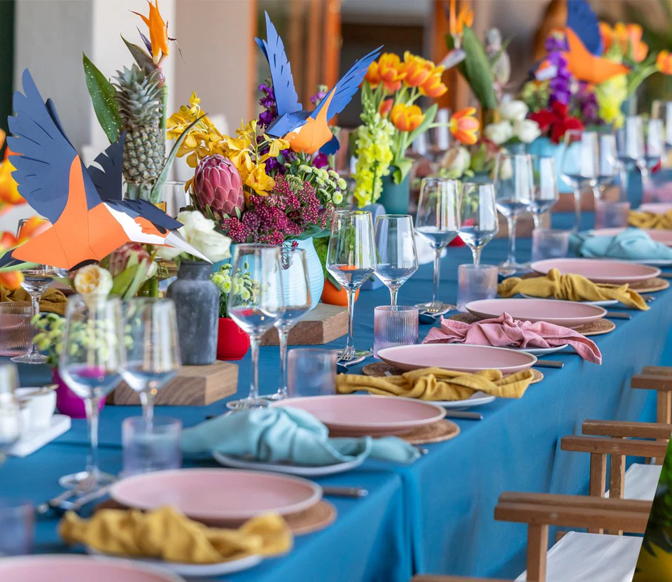 A long banquet table with paper kingfishers among the flowers