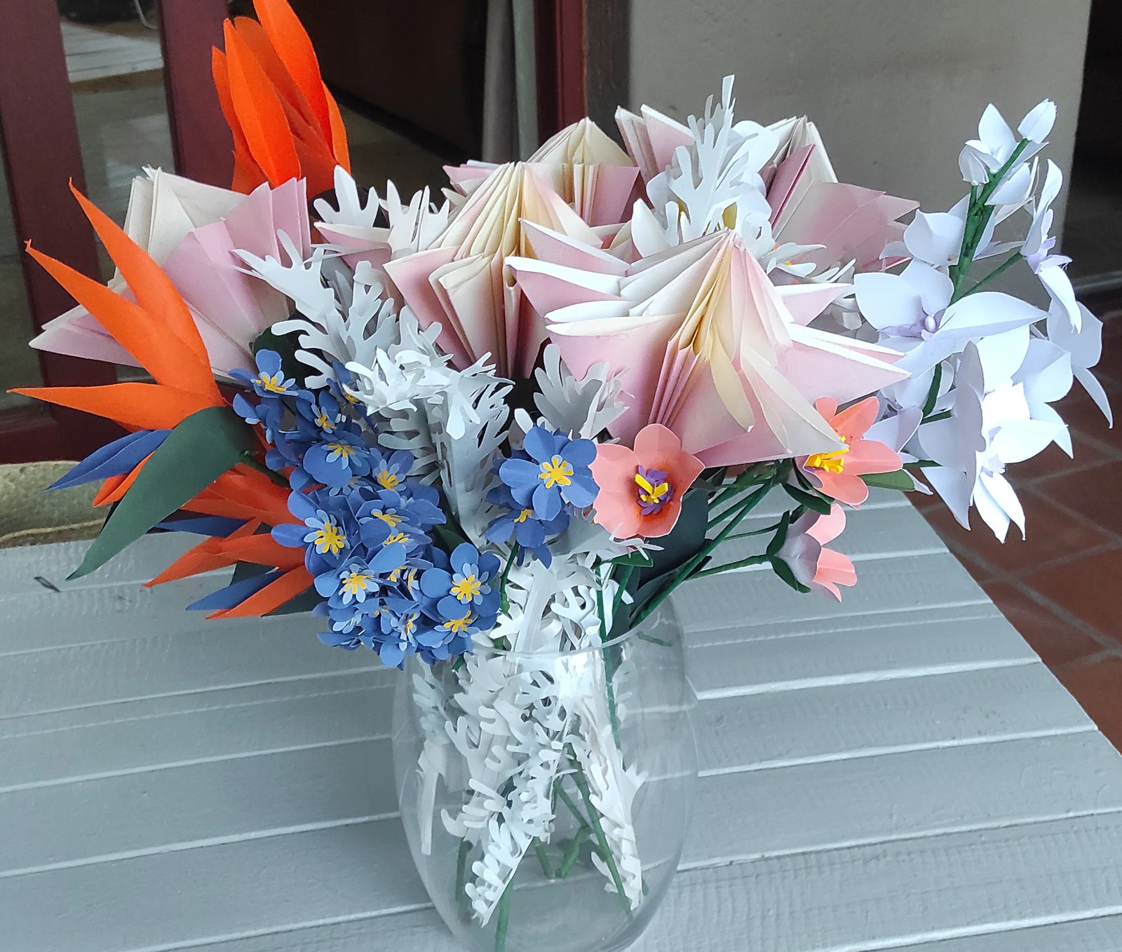 A table arrangement of paper lilies, strelitzia and blue blossom in a glass vase