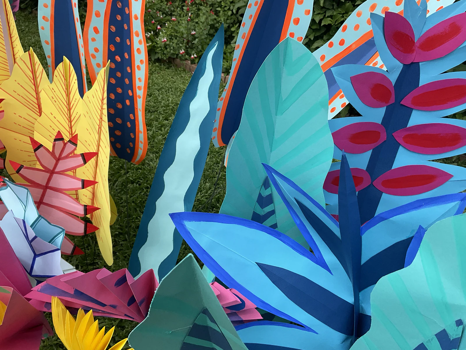 Hand-painted paper leaves in teal, magenta, yellow and blue, standing in a garden
