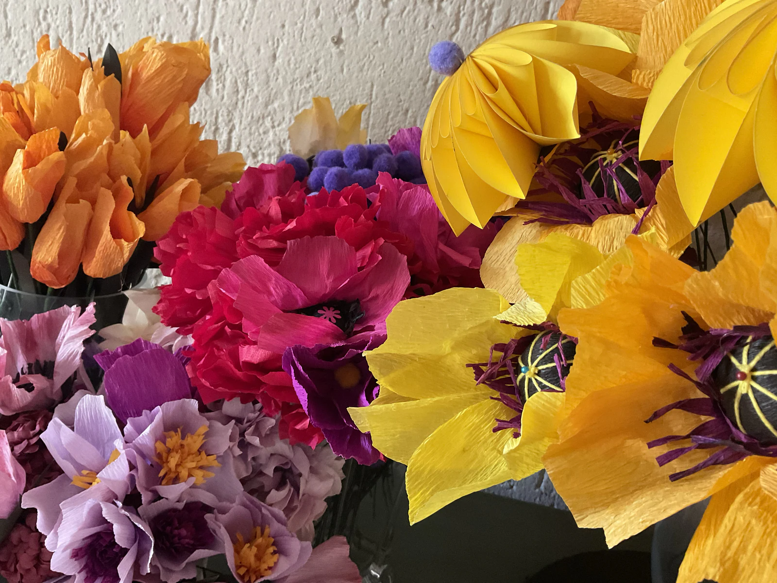 Bouquets of crepe paper poppies, carnations and anemones in yellow, magenta and lilac