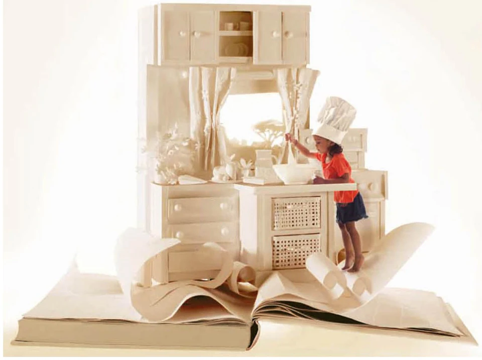 A paper kitchen rising out of an open book, with a child in a chef's hat
