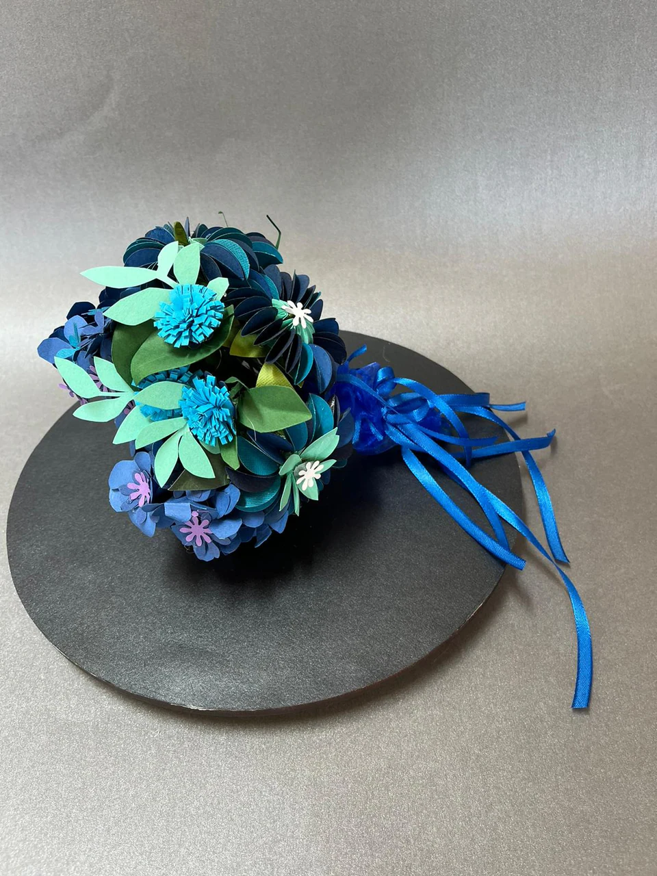 A headpiece of layered paper cornflowers in blues and teals with ribbon