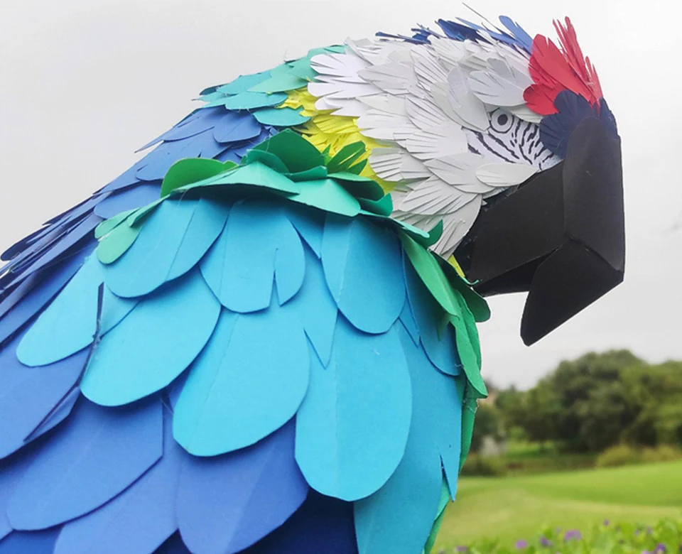 Close-up of a paper macaw, every feather cut separately in blues, greens and white