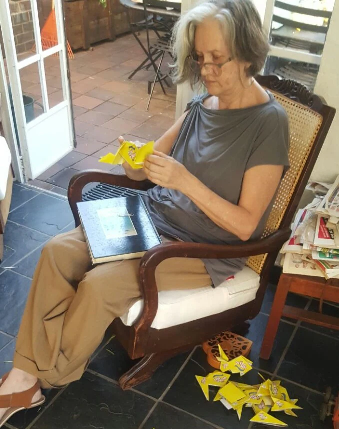 Hazel in a rocking chair, folding a piece of yellow origami